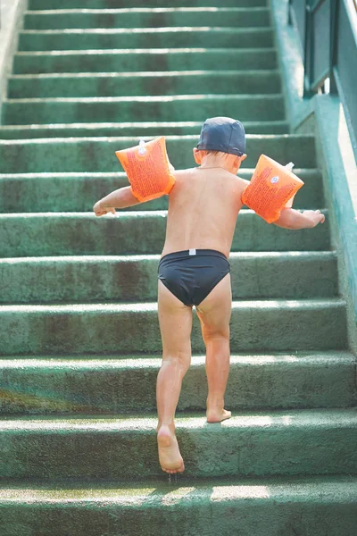 Bambino in braccioli per nuotare in una piscina all'aperto con scivolo d'acqua . — Foto Stock