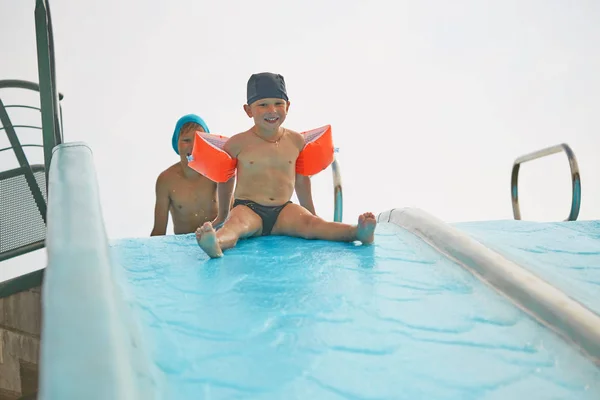 Niño en brazaletes para nadar en una piscina al aire libre con tobogán acuático . —  Fotos de Stock