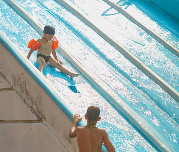 Enfant dans des brassards pour nager dans une piscine extérieure avec toboggan aquatique . — Photo