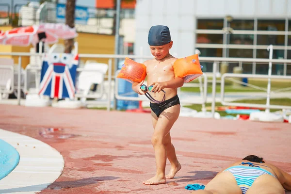 Enfant dans des brassards pour nager dans une piscine extérieure avec toboggan aquatique . — Photo