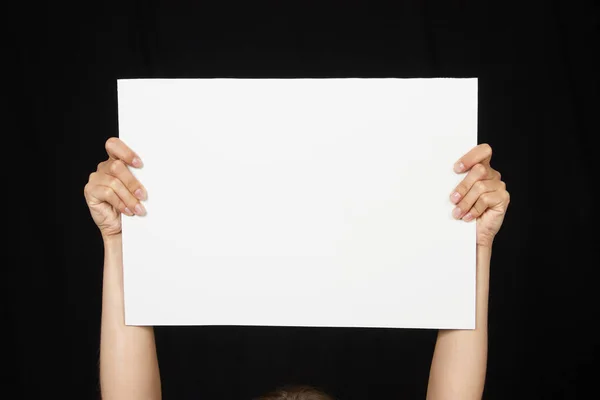 Manos femeninas sosteniendo hoja de papel en blanco aisladas en negro — Foto de Stock