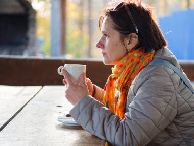 Kız açık havada beyaz bir bardaktan kahve içiyor.