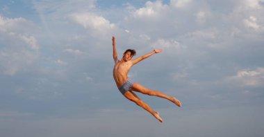 Sahilde atletik bir genç, denizin ve gökyüzünün arka planında zıplıyor.