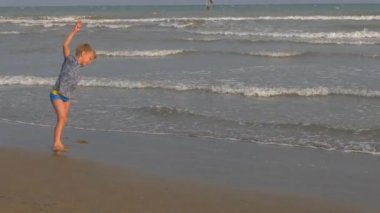 Sahildeki atletik çocuk denizin ve gökyüzünün arka planında zıplıyor.