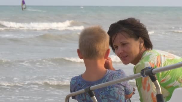 Mamá abraza hijo en la orilla del mar en el viento — Vídeo de stock