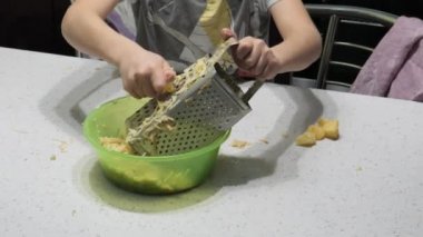 Küçük oğlan yemek hazırlıyor. Patates ovuyor.