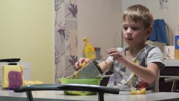 De kleine jongen bereidt eten. aardappelen inwrijven — Stockvideo