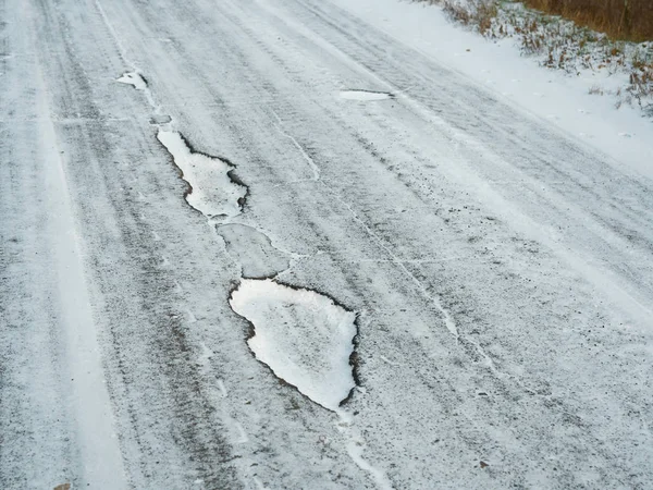 Primeira neve. Pothole poços em uma estrada branca nevada — Fotografia de Stock