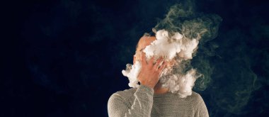 Sigara içen adam siyah arka planda sigara içiyor.