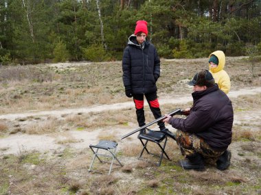 Adam çocuklara av tüfeğiyle ateş etmeyi öğretiyor.