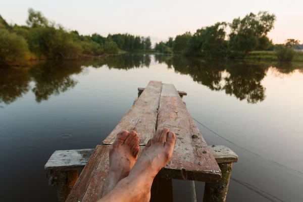 legs of a man resting by the pond in the rays at sunset day 2020