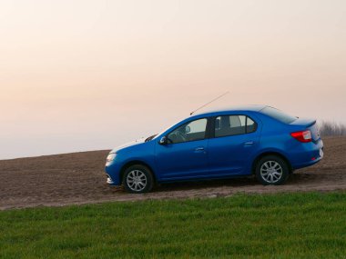 Gomel, Belarus - 8 Nisan 2020: Mavi Renault Logan arabası 2020 'de gün doğumunda bir tarlada.