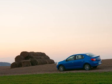 Gomel, Belarus - 8 Nisan 2020: Mavi Renault Logan arabası 2020 'de gün doğumunda bir tarlada.