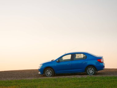 Gomel, Belarus - 8 Nisan 2020: Mavi Renault Logan arabası 2020 'de gün doğumunda bir tarlada.
