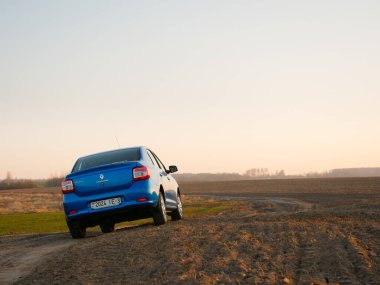 Gomel, Belarus - 8 Nisan 2020: Mavi Renault Logan arabası 2020 'de gün doğumunda bir tarlada.