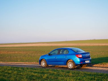 Gomel, Belarus - 8 Nisan 2020: Mavi Renault Logan arabası 2020 'de gün doğumunda bir tarlada.