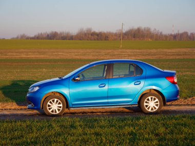 Gomel, Belarus - 8 Nisan 2020: Mavi Renault Logan arabası 2020 'de gün doğumunda bir tarlada.
