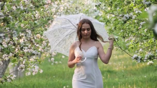 庭でリンゴの木を咲かせている白い傘の女の子 — ストック動画