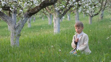 2020 'de bahçede çimlerin üzerinde çiçek açan elma ağaçlarının yanında bir çocuk.