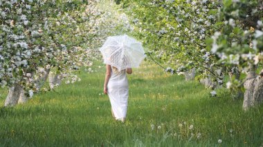 2020 bahçesinde çiçek açan elma ağaçlarında beyaz şemsiyeli bir kız.