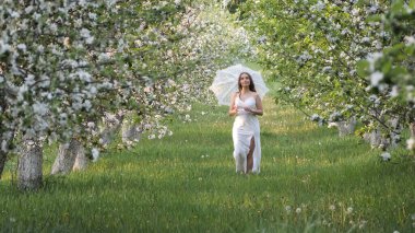 2020 bahçesinde çiçek açan elma ağaçlarında beyaz şemsiyeli bir kız.