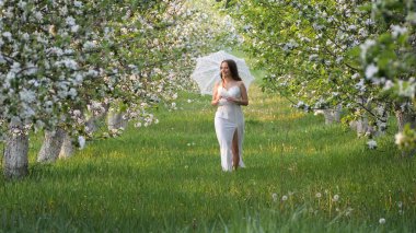 2020 bahçesinde çiçek açan elma ağaçlarında beyaz şemsiyeli bir kız.