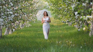 2020 bahçesinde çiçek açan elma ağaçlarında beyaz şemsiyeli bir kız.