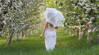 2020 bahçesinde çiçek açan elma ağaçlarında beyaz şemsiyeli bir kız.
