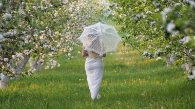 2020 bahçesinde çiçek açan elma ağaçlarında beyaz şemsiyeli bir kız.
