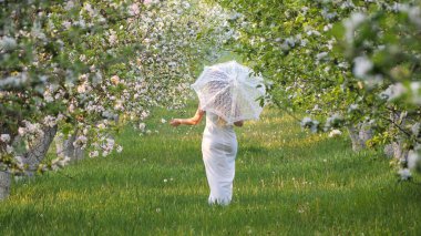 2020 bahçesinde çiçek açan elma ağaçlarında beyaz şemsiyeli bir kız.