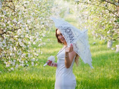 2020 bahçesinde çiçek açan elma ağaçlarında beyaz şemsiyeli bir kız.