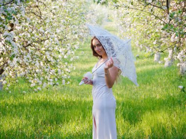 2020 bahçesinde çiçek açan elma ağaçlarında beyaz şemsiyeli bir kız.