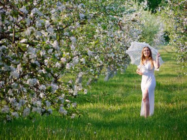2020 bahçesinde çiçek açan elma ağaçlarında beyaz şemsiyeli bir kız.