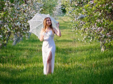 2020 bahçesinde çiçek açan elma ağaçlarında beyaz şemsiyeli bir kız.