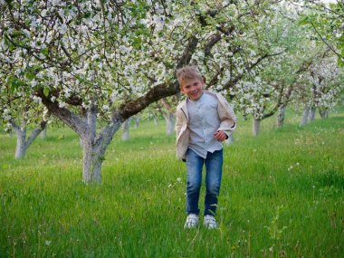 2020 'de bahçede çimlerin üzerinde çiçek açan elma ağaçlarının yanında bir çocuk.
