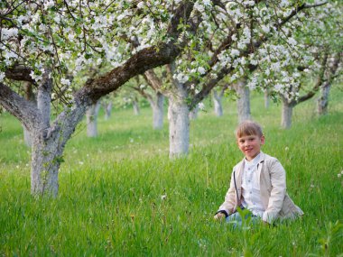 2020 'de bahçede çimlerin üzerinde çiçek açan elma ağaçlarının yanında bir çocuk.