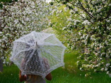 2020 bahçesinde çiçek açan elma ağaçlarında beyaz şemsiyeli bir kız.