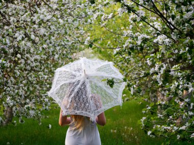 2020 bahçesinde çiçek açan elma ağaçlarında beyaz şemsiyeli bir kız.