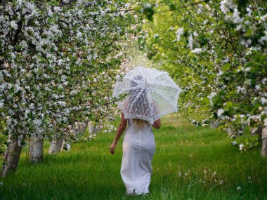 2020 bahçesinde çiçek açan elma ağaçlarında beyaz şemsiyeli bir kız.
