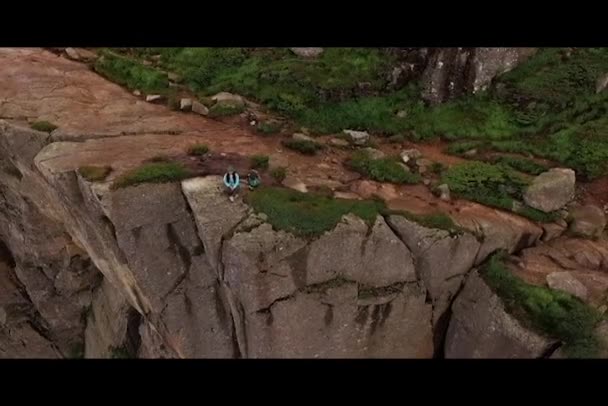 Noruega. Las montañas. Una chica se sienta en el borde del acantilado. Vista desde el dron — Vídeos de Stock