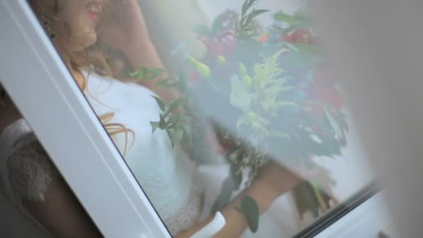 Невеста с букетом стоит у открытого окна — стоковое видео