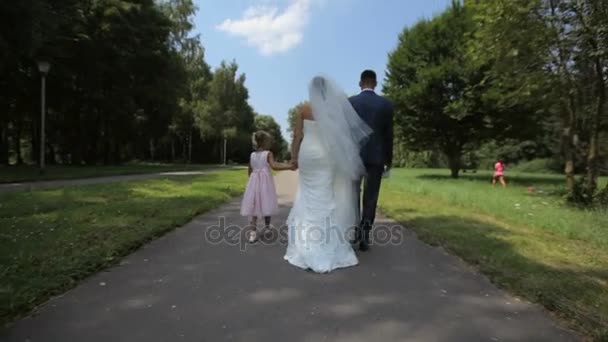 Bruid en bruidegom met meisje lopen in het park — Stockvideo