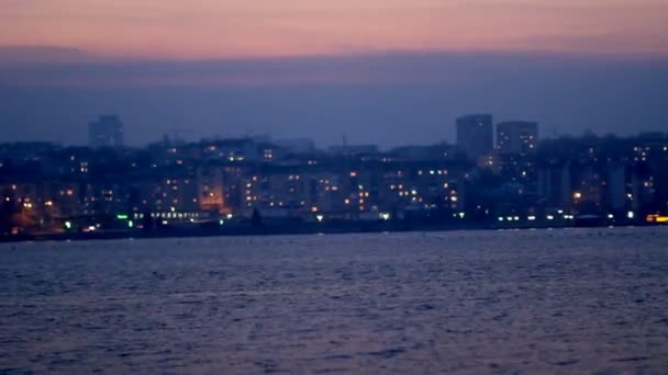 Ночной город с огнями на фоне озера и ночного неба — стоковое видео