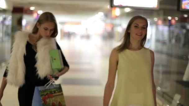Dziewczyna z bezprzewodowych słuchawek w sklepie. Zalety nowych technologii. Dwa womans szczęśliwy po zakupy z torby w centrum handlowym. Dziewczyny, zakupy. — Wideo stockowe