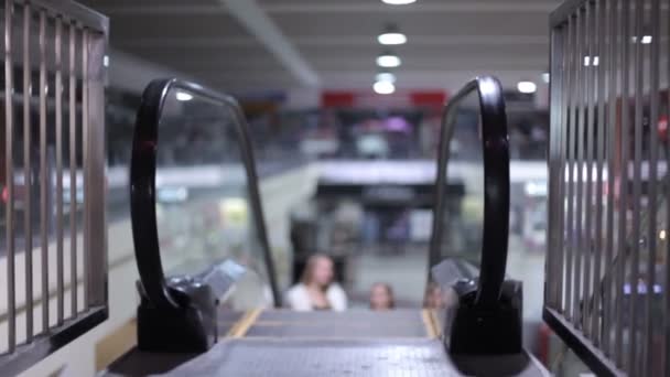 Fille avec casque sans fil est debout sur un escalier roulant dans un centre commercial. Avantages des nouvelles technologies. Femme heureuse après avoir magasiné avec des sacs à provisions dans un centre commercial . — Video