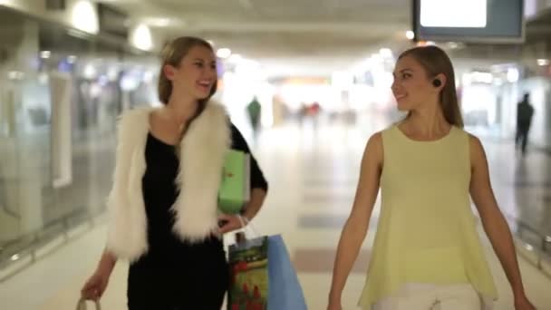 Depodaki kablosuz kulaklık kız. Yeni teknolojiler avantajları. Elinde çanta alışveriş merkezinde alışveriş sonra iki kadının mutlu. Kız alışveriş. — Stok video