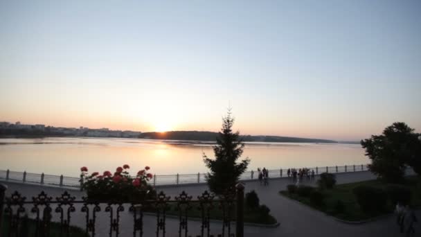 Prachtig uitzicht op het meer en de waterkant bij zonsondergang. Mensen lopen op de pittoreske Dijk bij zonsondergang — Stockvideo