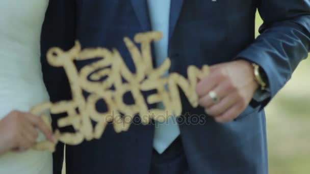 Recién casados felices sosteniendo una pancarta de madera recién casados. Retrato de una feliz pareja de recién casados. día de la boda — Vídeos de Stock