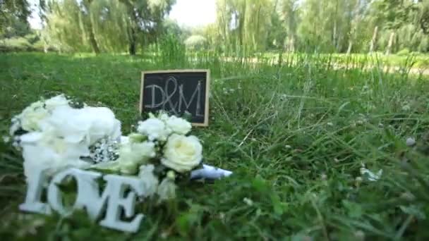 Ślubna dekoracja słowo miłość, kwiaty i Drewniana tablica z litery D i M na tle zielonej trawie w parku — Wideo stockowe