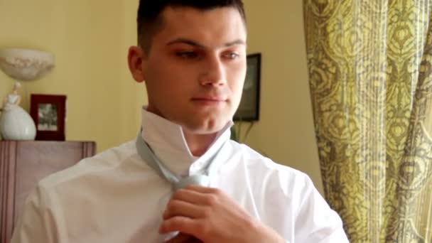 Красивый парень одевает галстук и улыбается. В день свадьбы. Жених носит галстук — стоковое видео